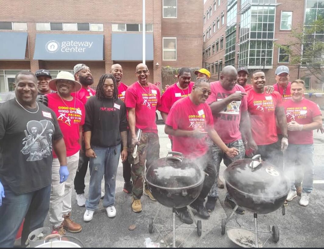Friends Giving Back volunteers in red shirts around smoking grills at the Gateway Center cookout